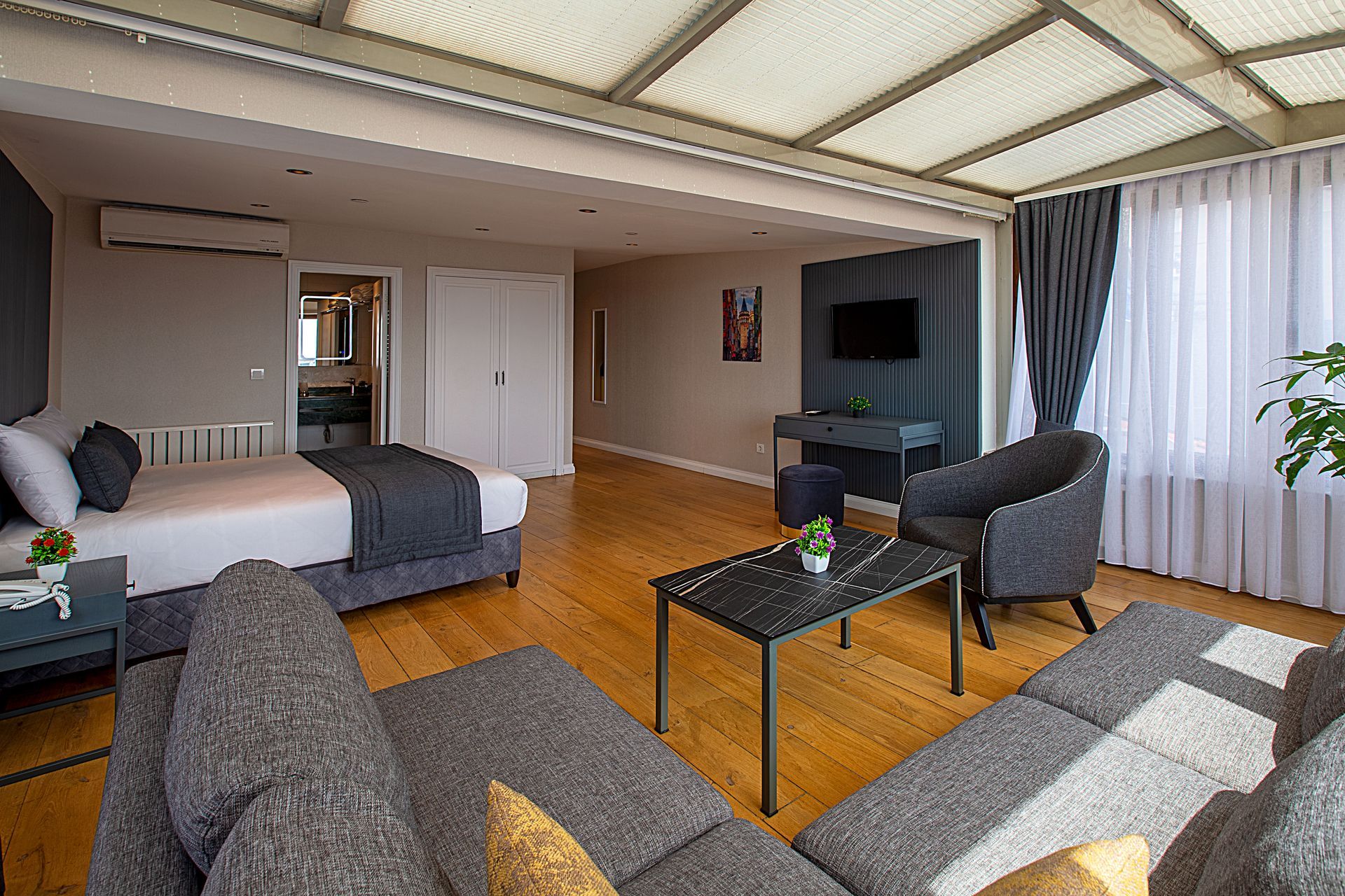 Modern hotel room with bed, sofa, TV, and glass coffee table on wood floors