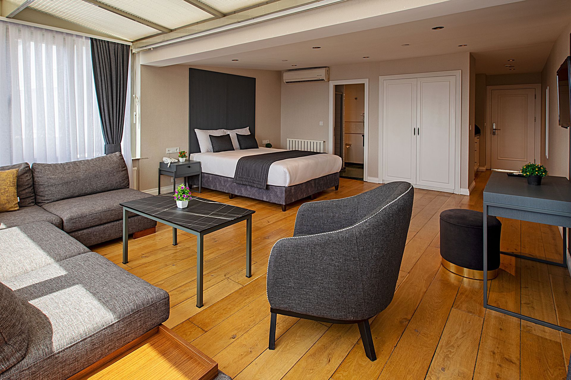 Spacious bedroom with a bed, sofa, chair, desk, and wood floor in a modern loft-style room