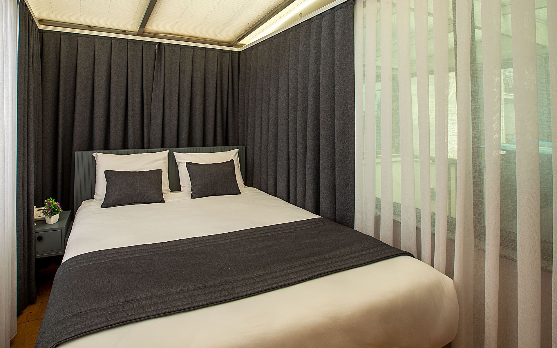 Modern bedroom with a neatly made bed, dark curtains, and floor-to-ceiling vertical blinds