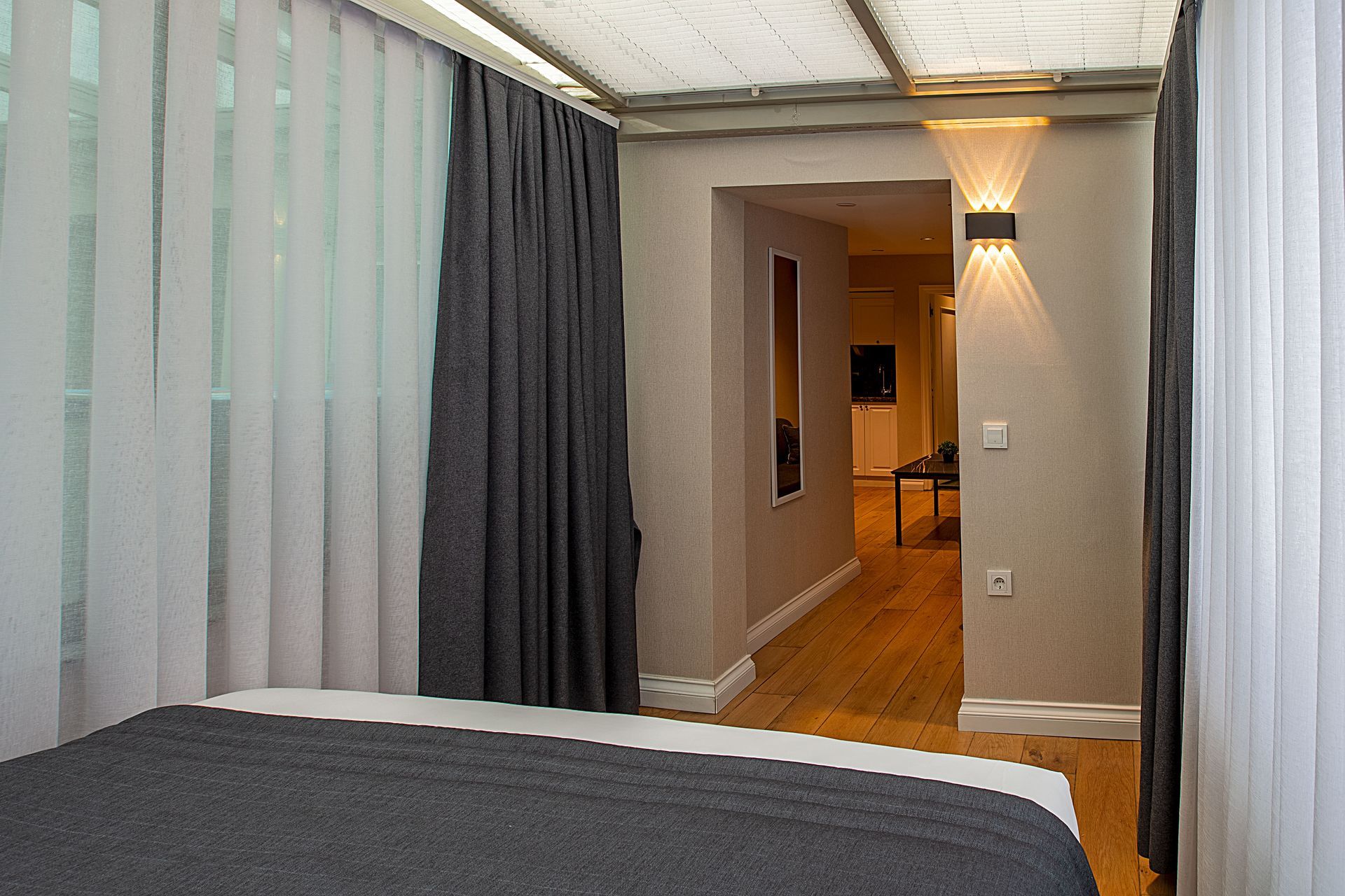 Modern bedroom with bed, striped curtains, and a hallway leading to a lit living area