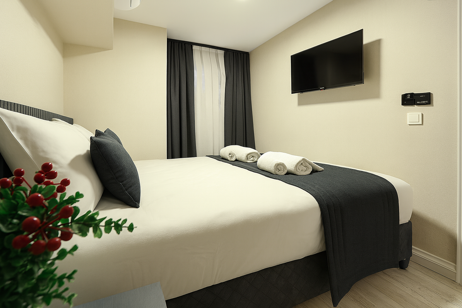 Small modern bedroom with a made bed, wall-mounted TV, and dark curtains.