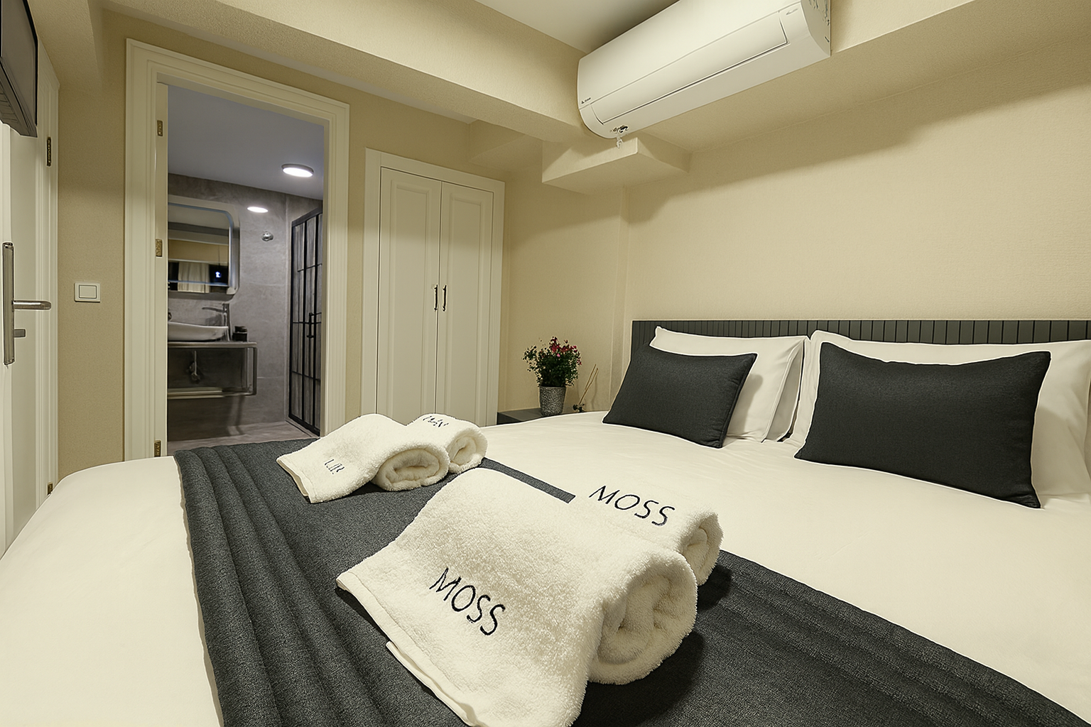 Modern bedroom with a neatly made bed, dark gray bedding, white walls, and an air conditioner above the headboard