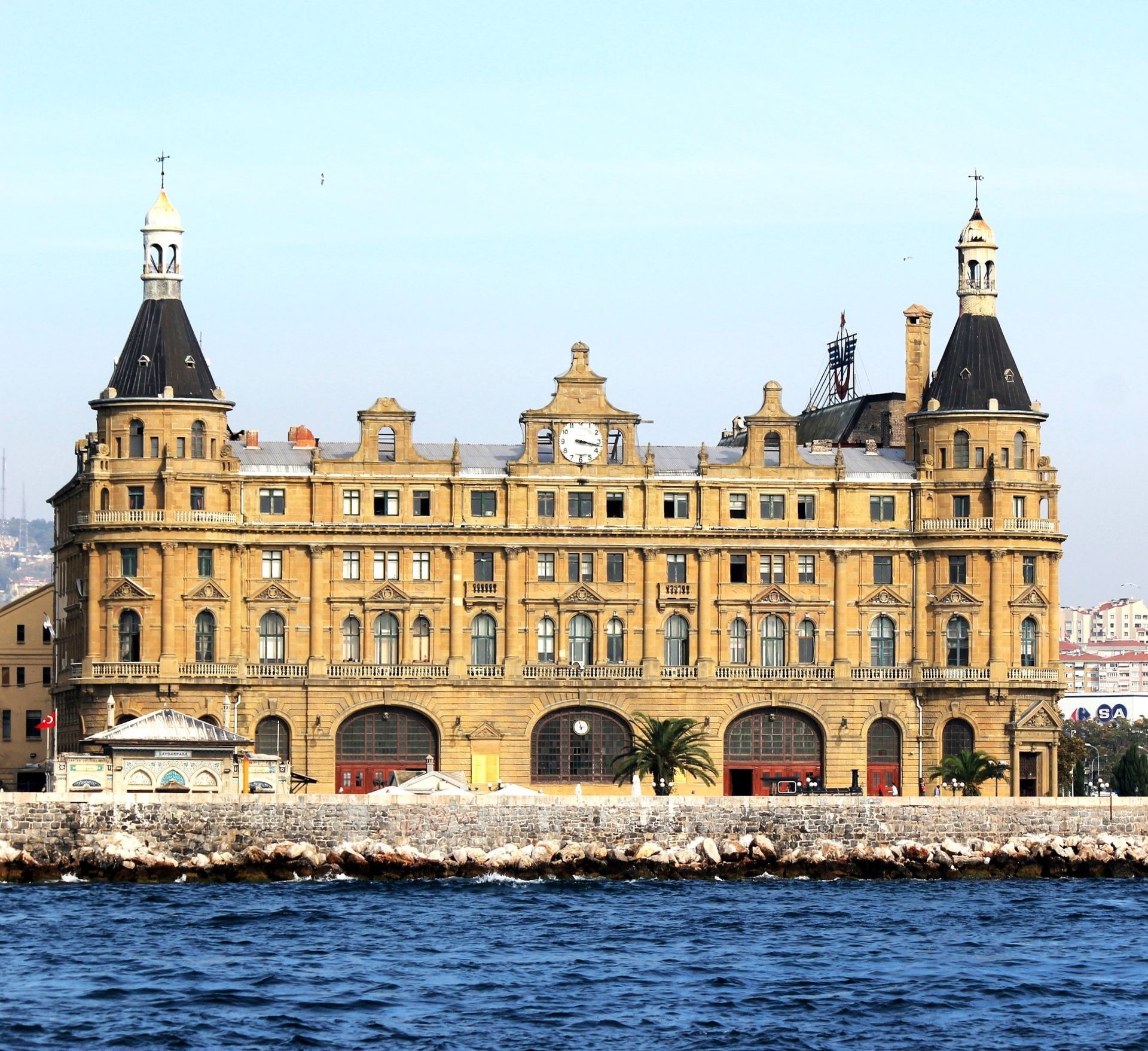 Haydarpaşa Tren İstasyonu, İstanbul, Türkiye. Kuleleri, kemerli girişleri olan, su kıyısında yer alan bej ve kahverengi bina.