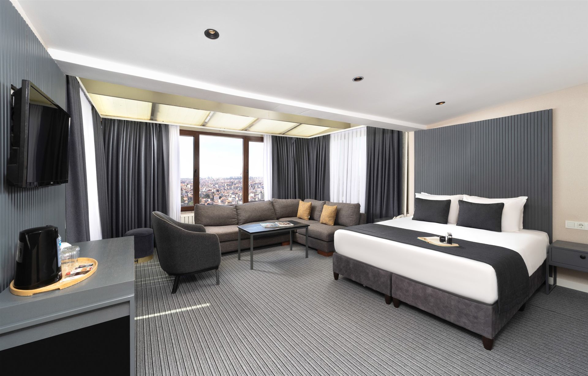 Spacious modern bedroom with a large bed, blue curtains, wooden floor, and city view windows.