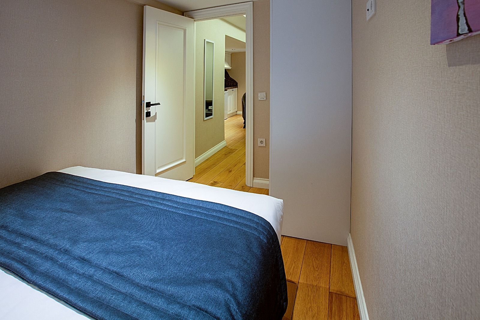 Small bedroom with blue bedspread and open doorway leading to a hallway.