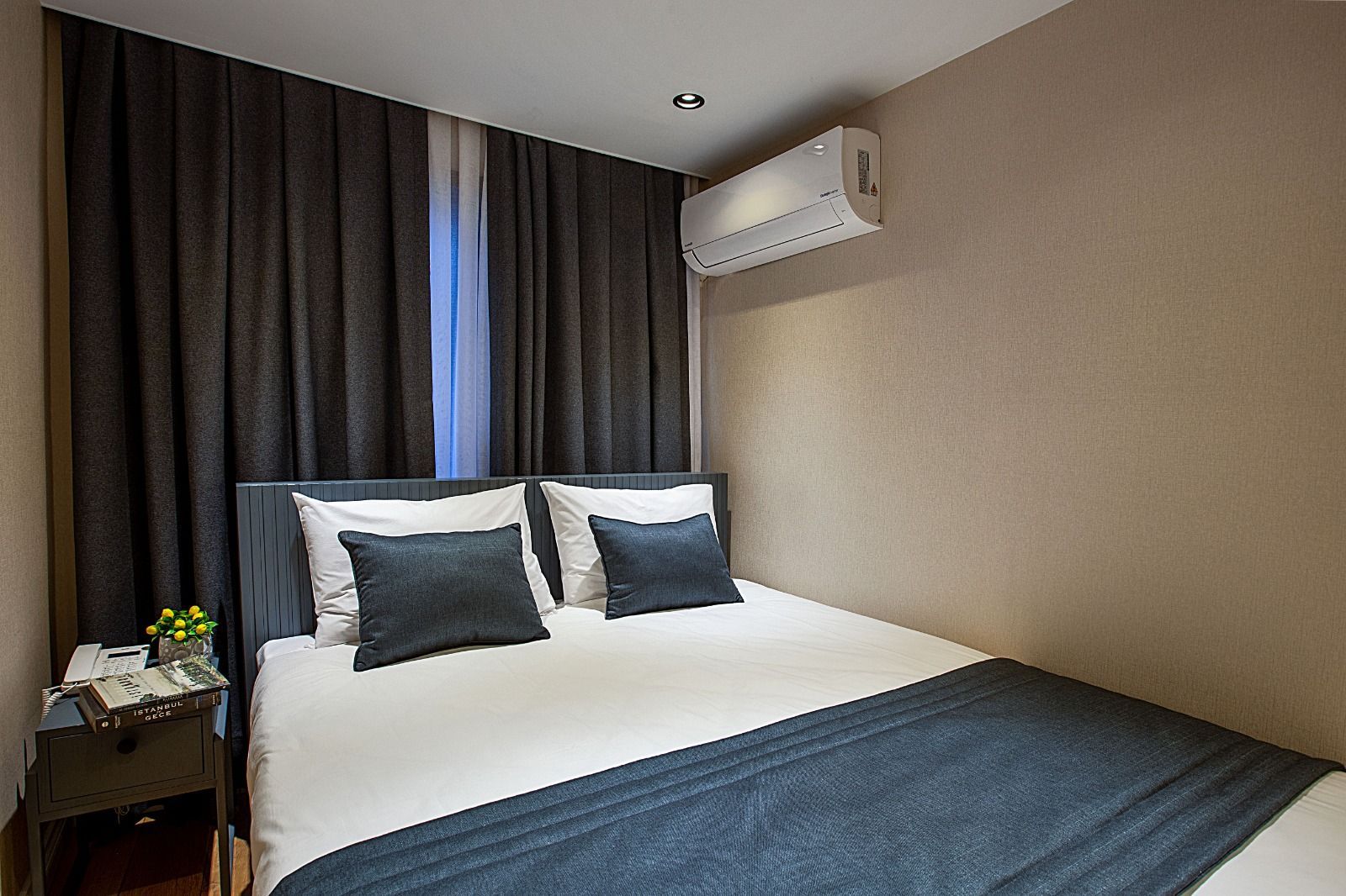 Neat modern bedroom with a white bed, dark pillows, gray curtains, and a wall-mounted air conditioner.