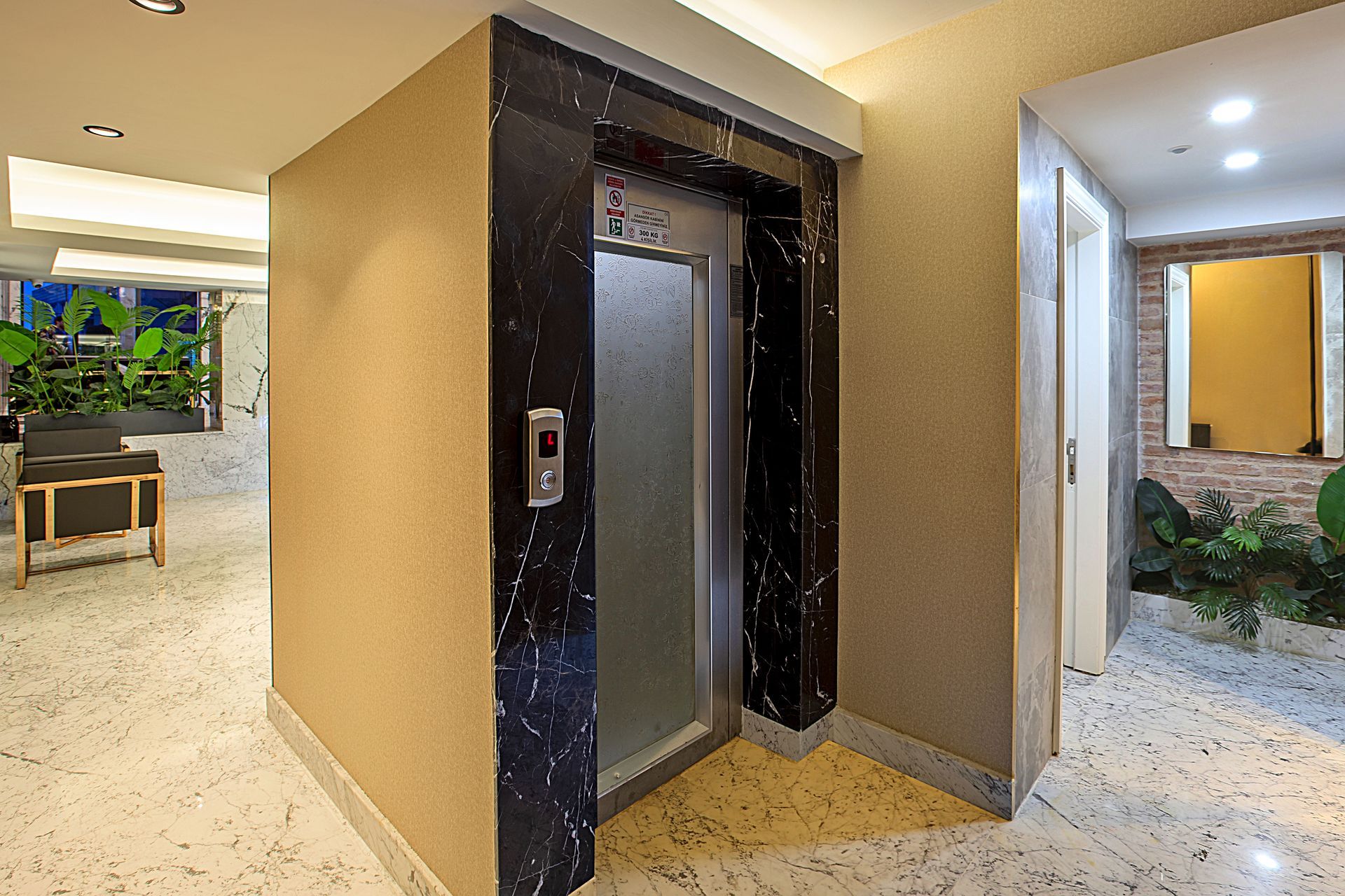 Modern building lobby with a central elevator, beige walls, and bright hallway seating areas