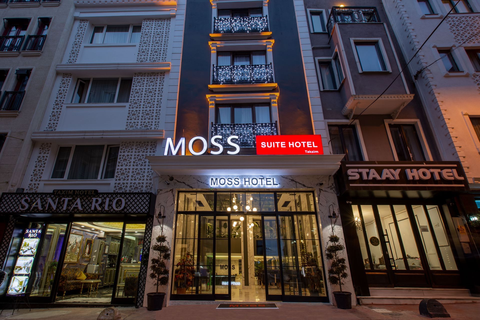 Hotel storefronts at dusk, with illuminated signs and glass entrances on a city street.