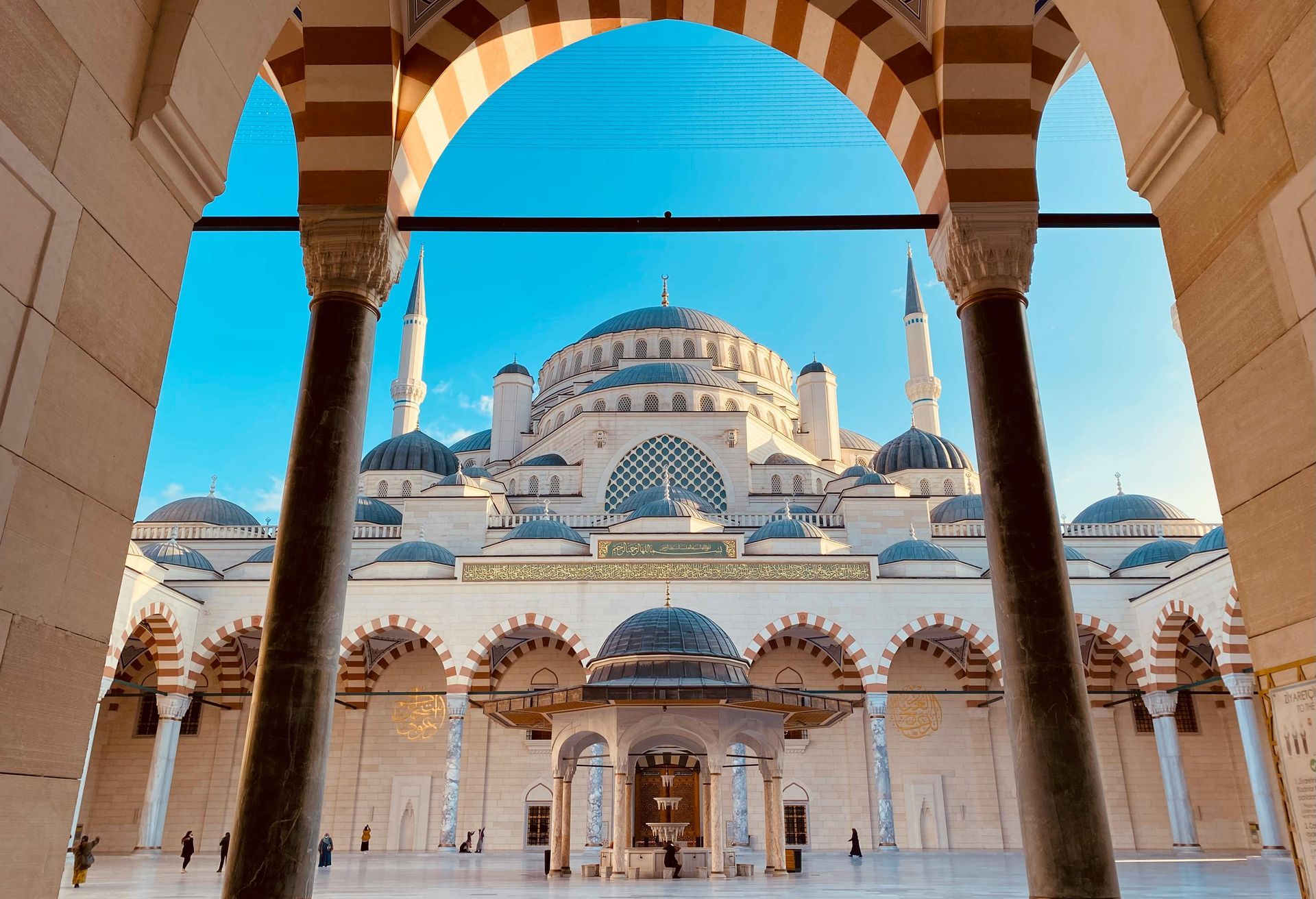 blue mosque courtyard framed by striped arches and columns under a bright blue sky