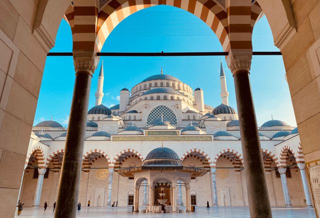 Kubbeleri, minareleri ve kemerli sütunlarıyla parlak mavi gökyüzüne karşı bir caminin görünümü.