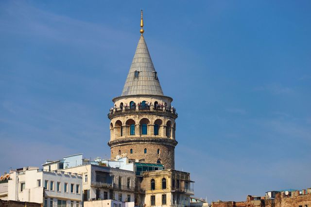 İstanbul, Türkiye'deki Galata Kulesi, mavi gökyüzünün önünde konik çatısı ve çevresindeki binalarla.