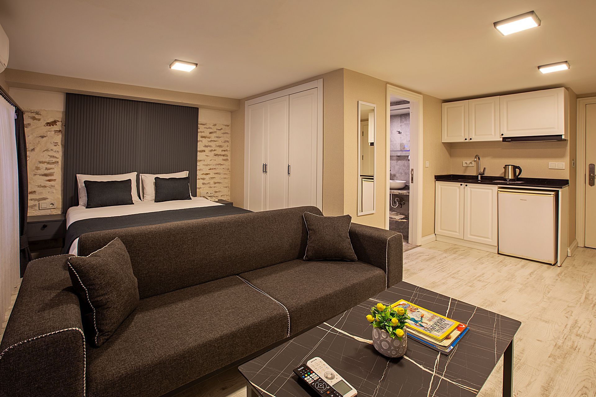 Modern living room with dark sectional sofa, coffee table, kitchenette, and bright recessed lighting
