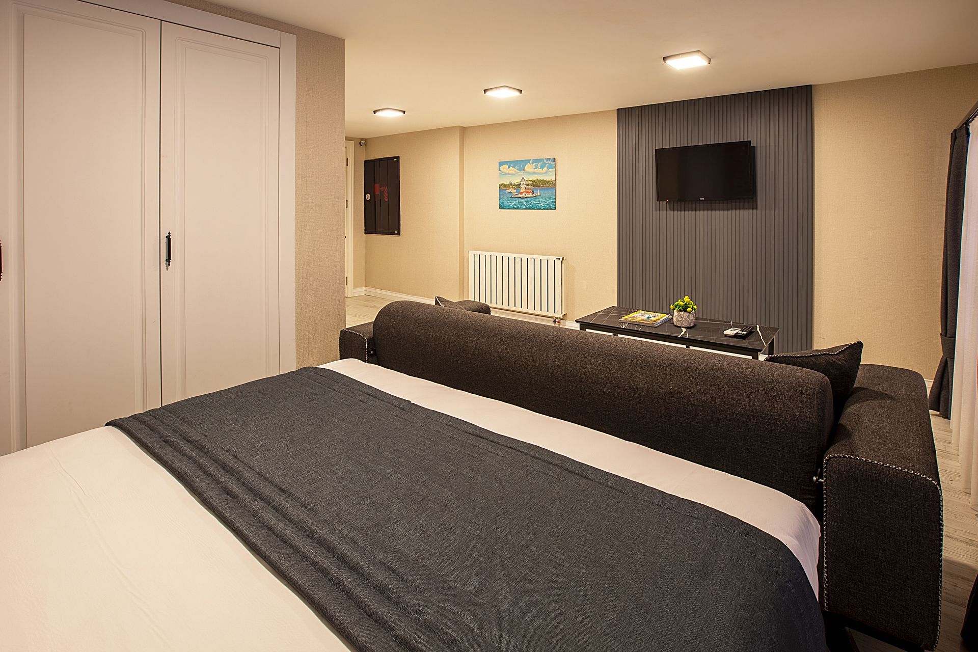 Modern bedroom with a bed, white closet doors, wall-mounted TV, and soft recessed lighting