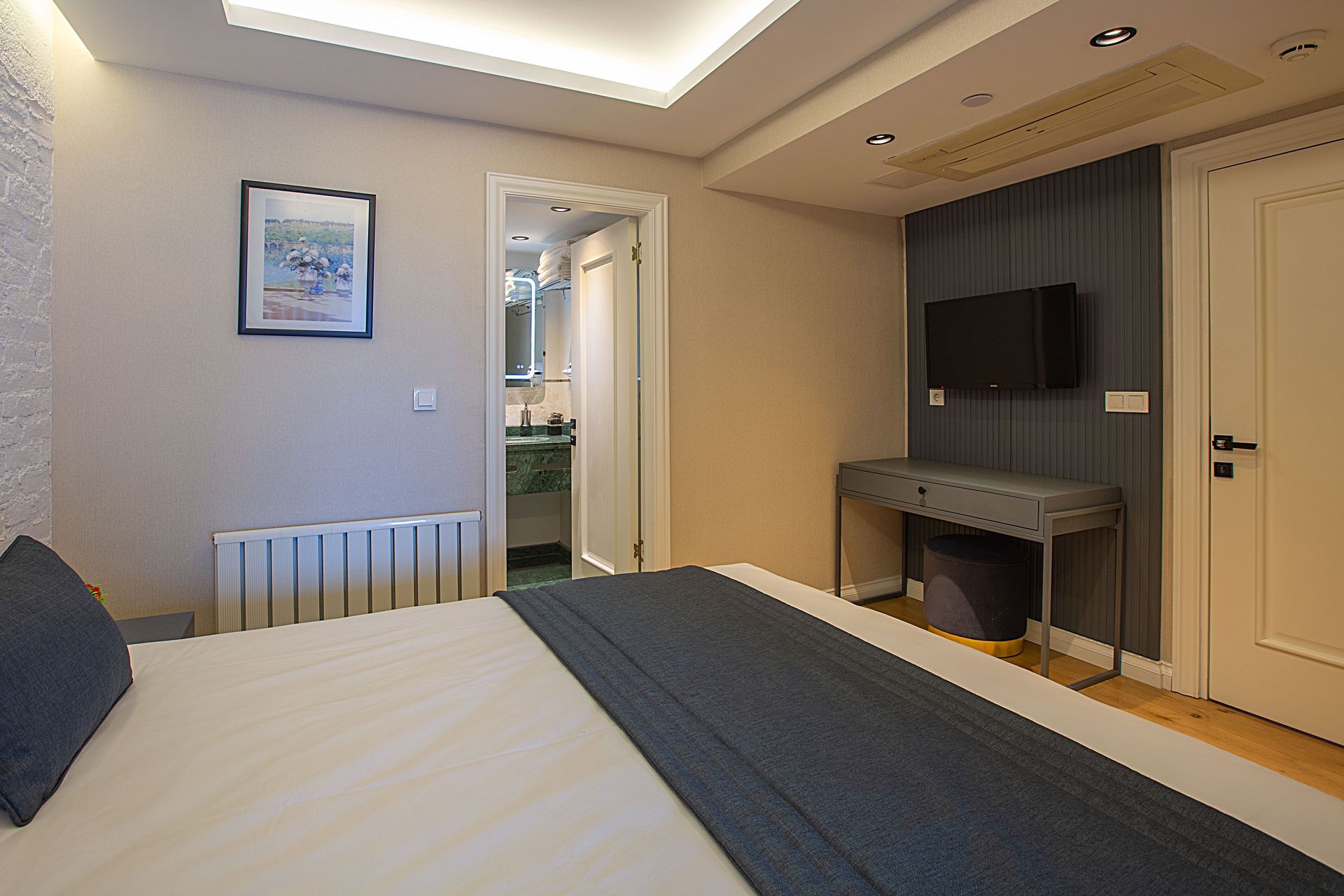 Modern bedroom with a bed, wall-mounted TV, desk, and open doorway to a bathroom