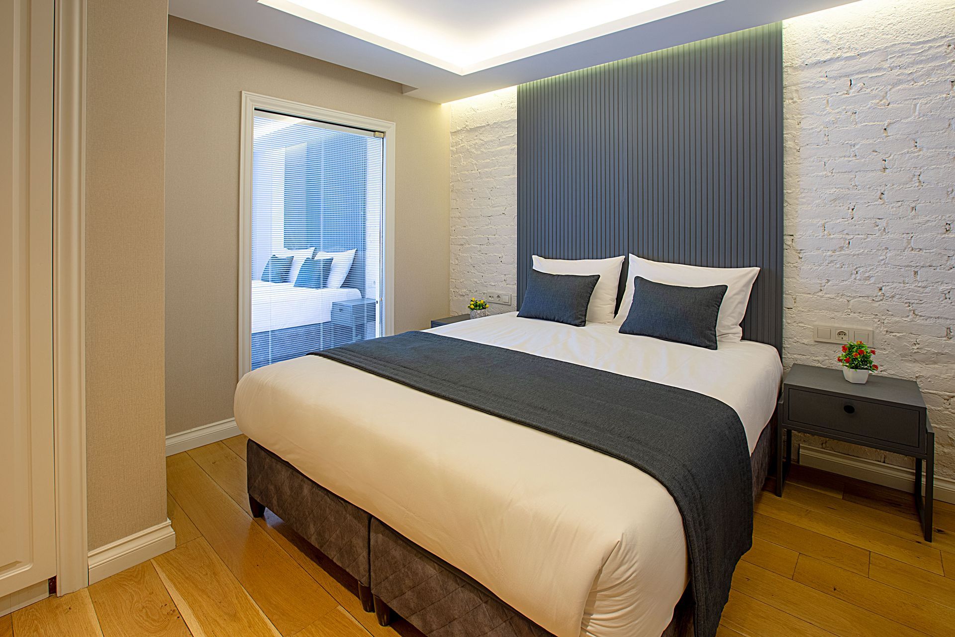 Modern bedroom with a neatly made bed, dark blue accents, wooden floor, and soft lighting