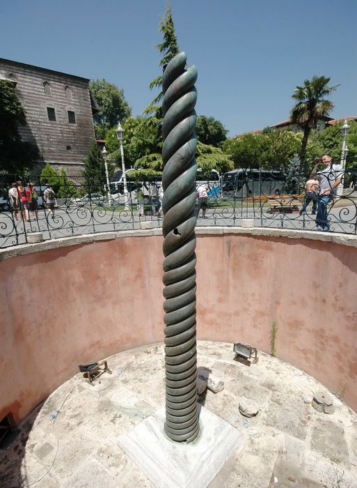 Arka planda insanlar ve binalar bulunan dairesel bir taş kaide