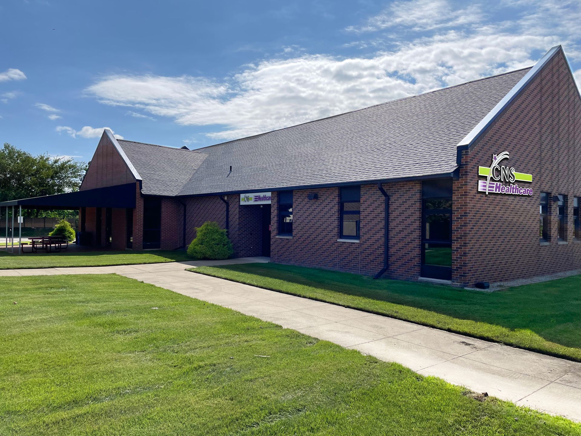 A large brick building with a gray roof is surrounded by lush green grass.