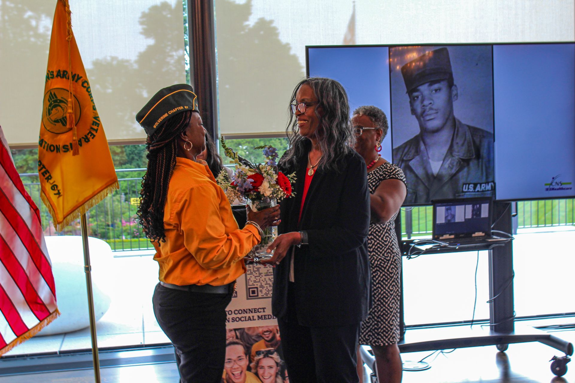A woman is giving a bouquet of flowers to another woman in front of a picture of a soldier.