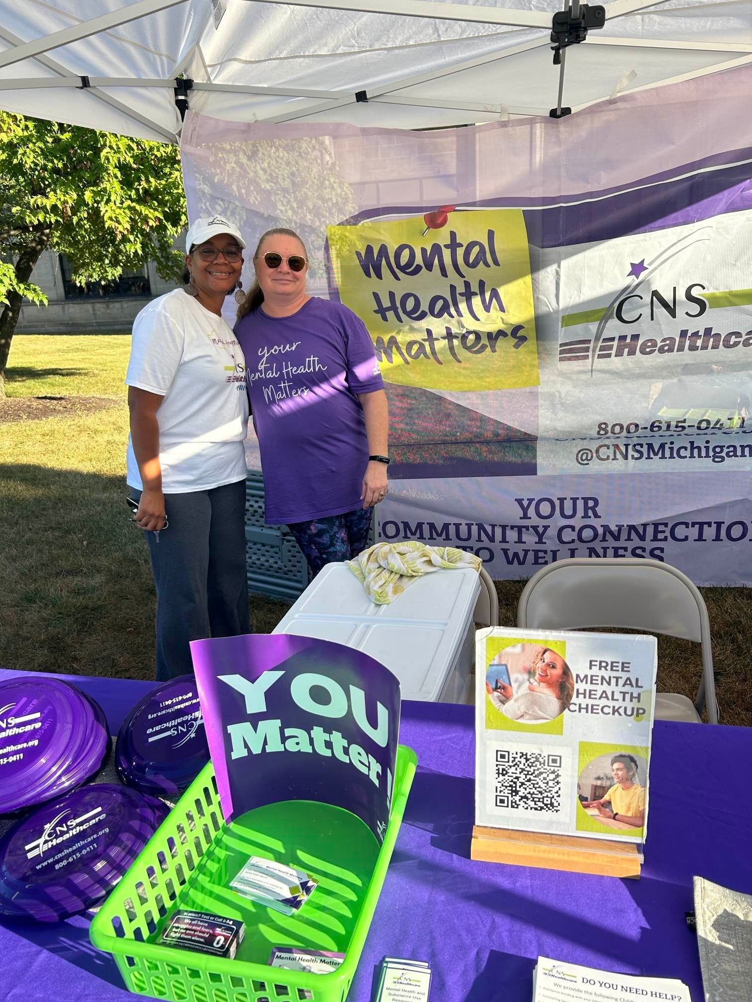 Two women are standing next to each other in front of a tent.