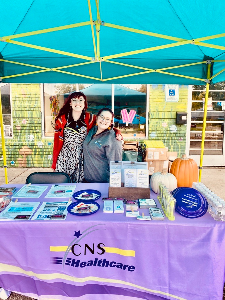 Two women are posing for a picture at a table under a tent.