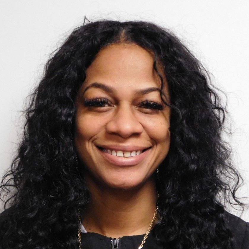 A woman with dreadlocks and glasses is smiling for the camera