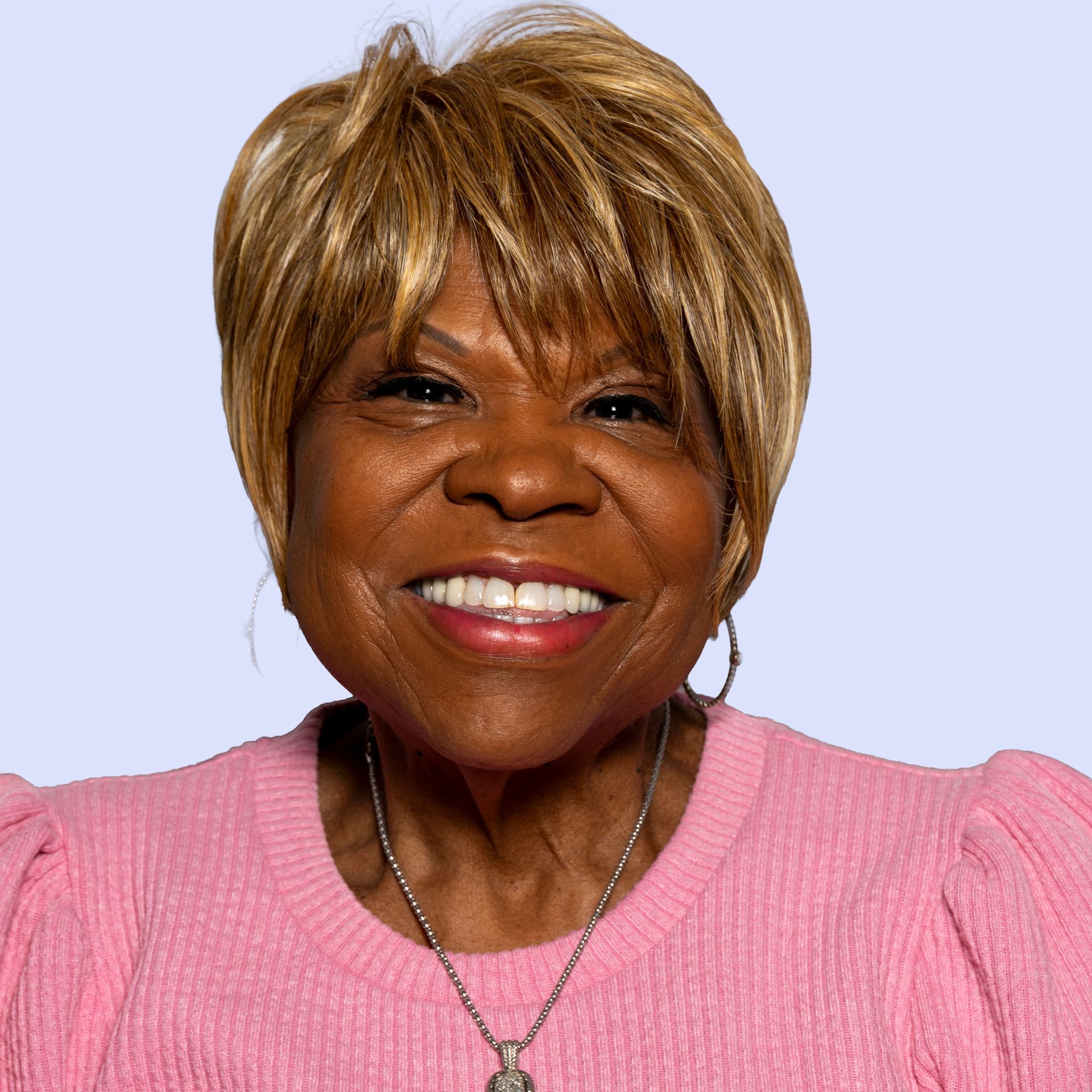 A woman wearing a red shirt and a pearl necklace smiles for the camera