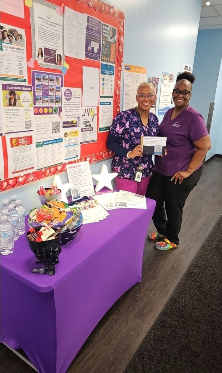 Two women are standing next to each other in front of a purple table.