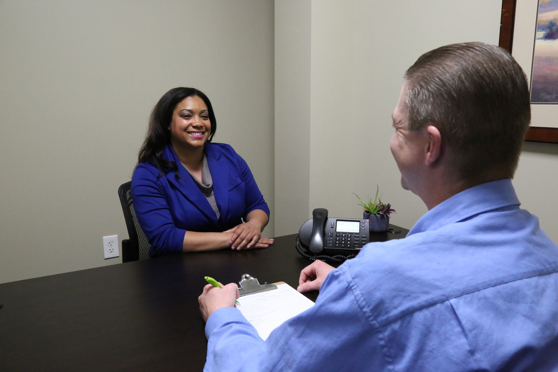 Woman in blue blazer smiles during an interview with a man in a blue shirt at a desk.