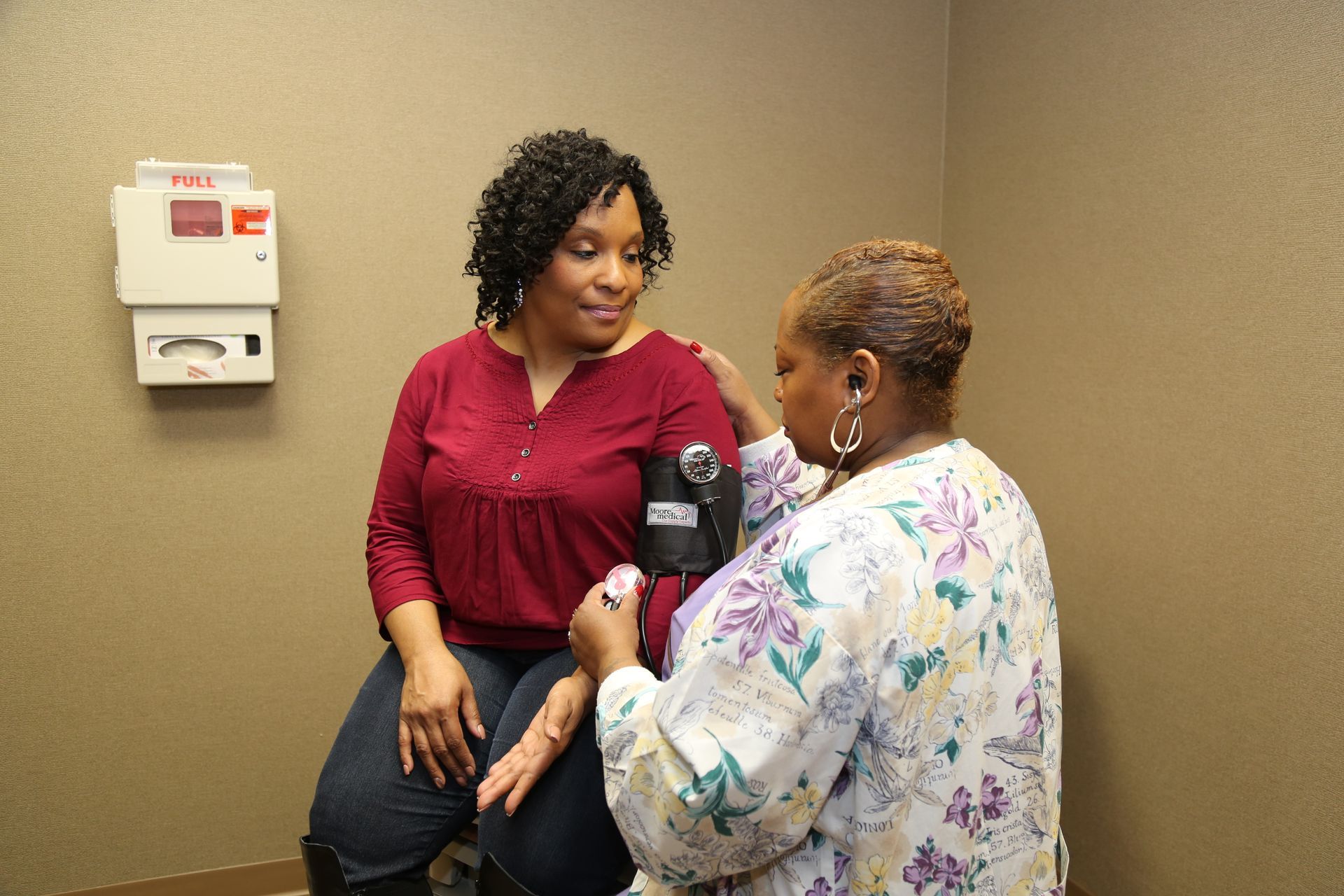 Nurse taking blood pressure of seated patient in a clinic room