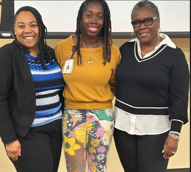 Three women posing for a picture with one wearing a name tag
