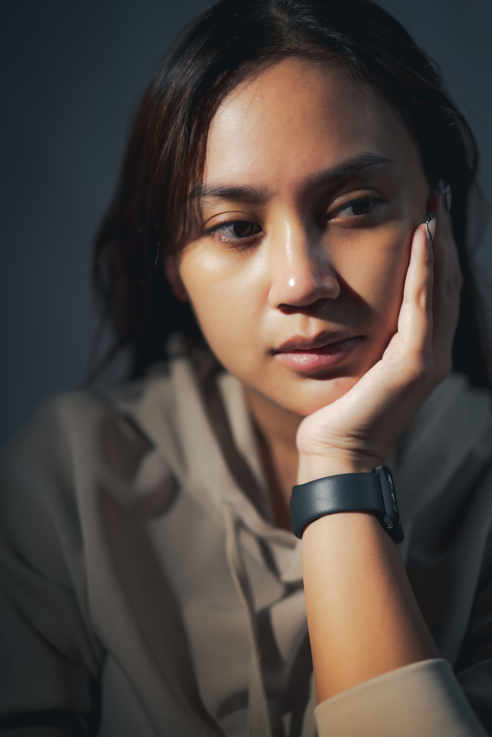 Portrait of a person resting their face on one hand, wearing a dark smartwatch, in soft side lighting
