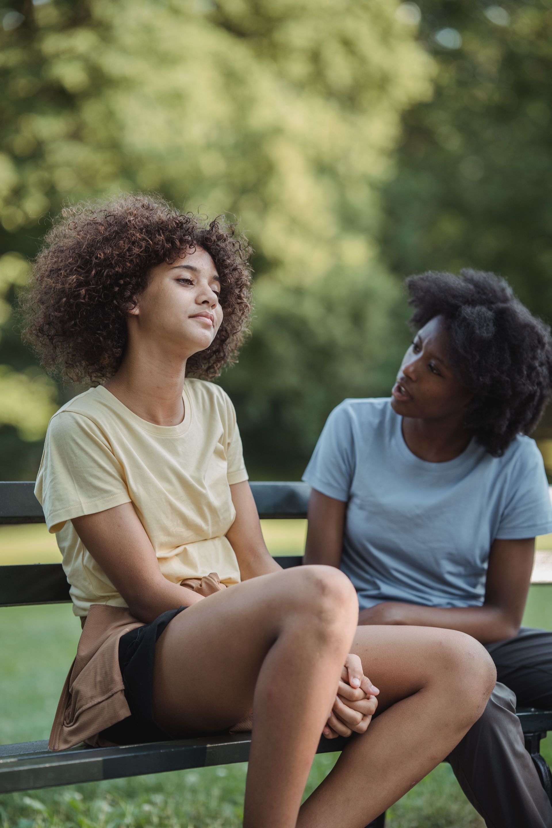 Mom and daughter sitting on a park bench, chatting in a green outdoor setting.