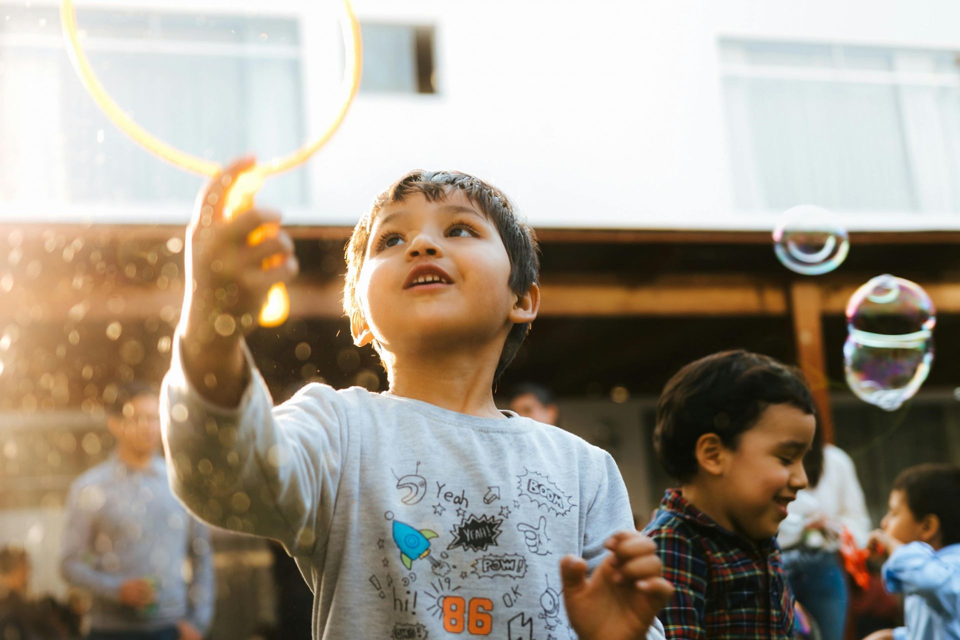 Child reaching for a bubble outdoors while others play in the background
