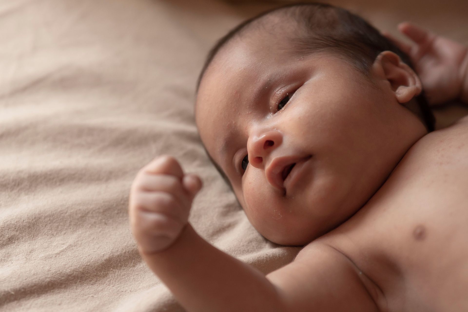 Sleeping baby lying on a beige blanket, with one hand raised near the face