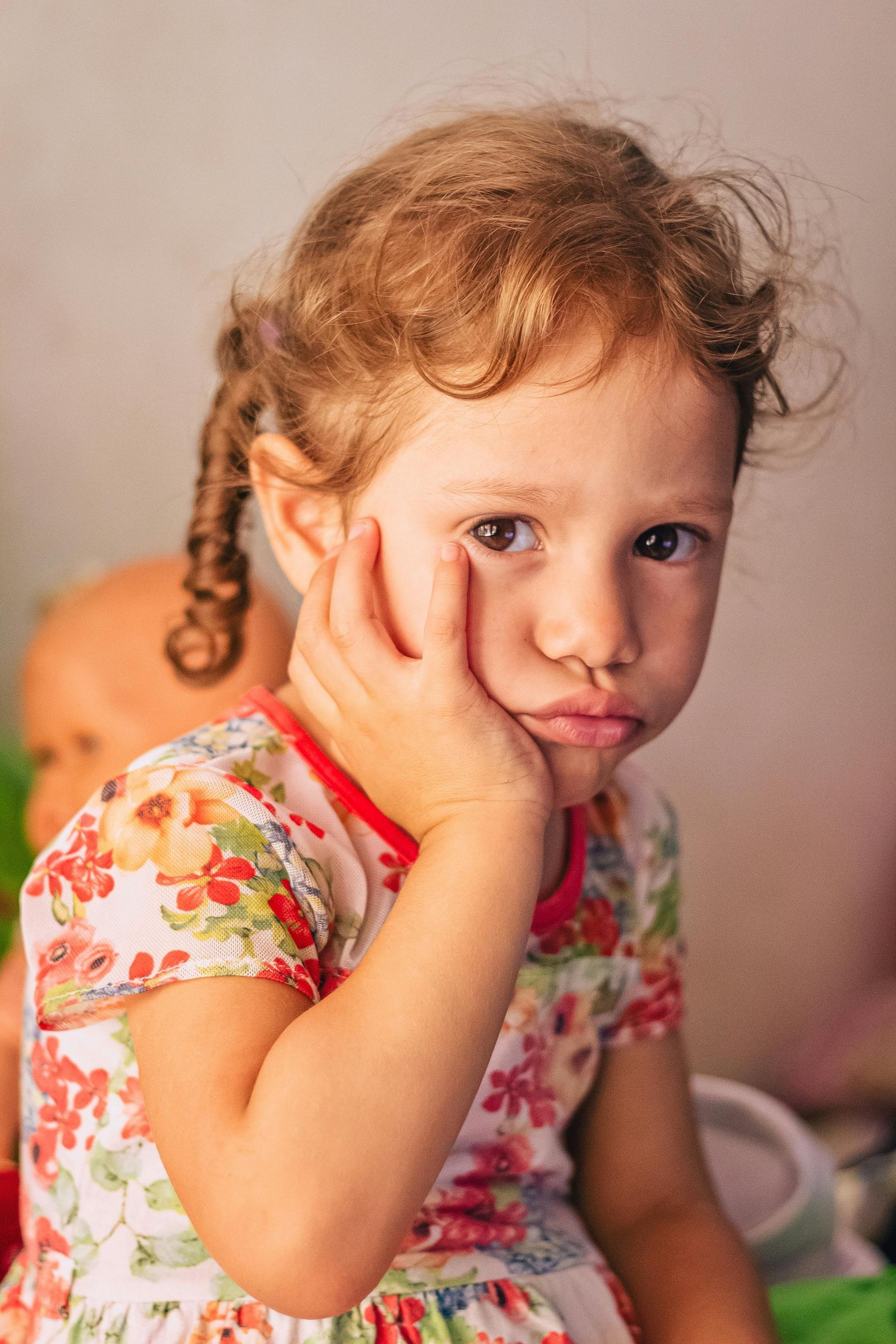 A little girl is sitting with her hand on her face.