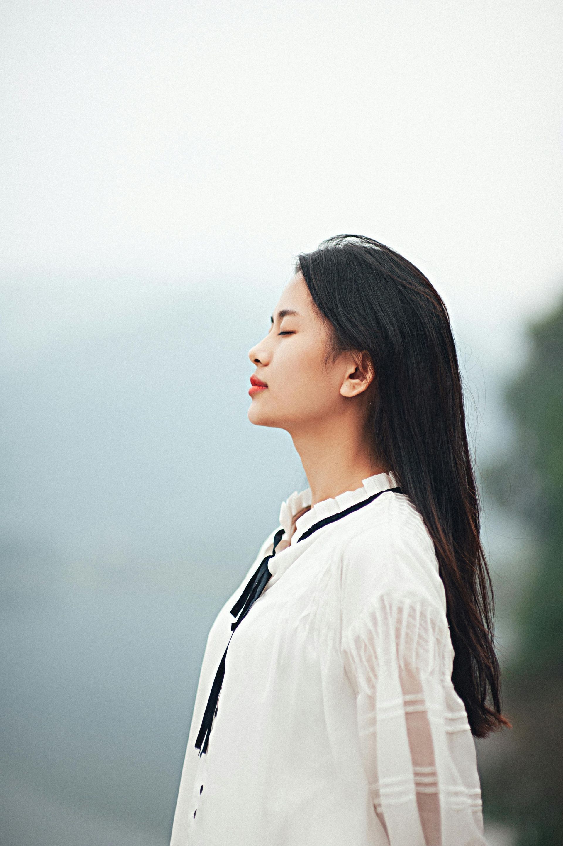 A woman breathing outside with eyes closed.