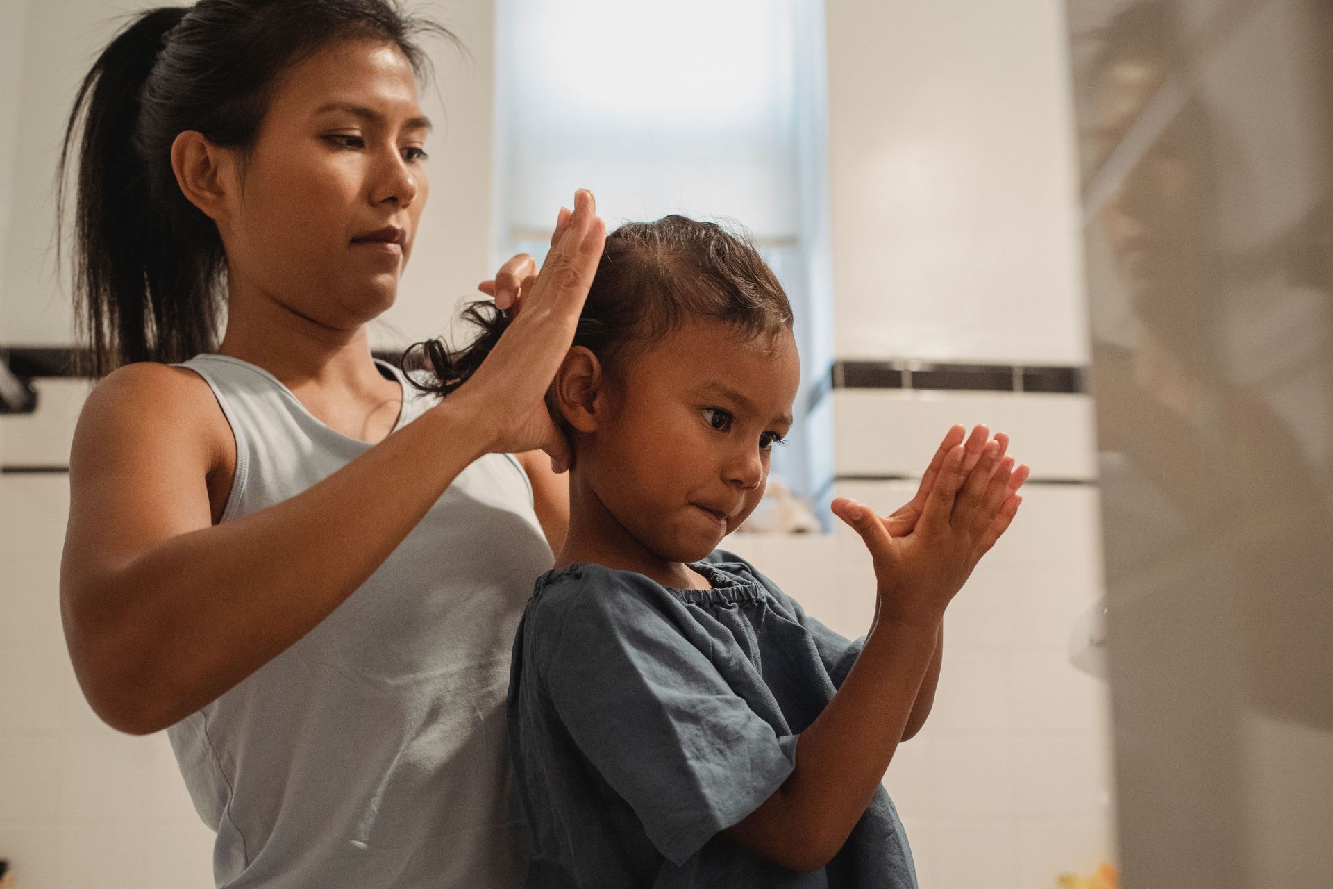 Two people standing indoors, one helping the other with a hair braid.