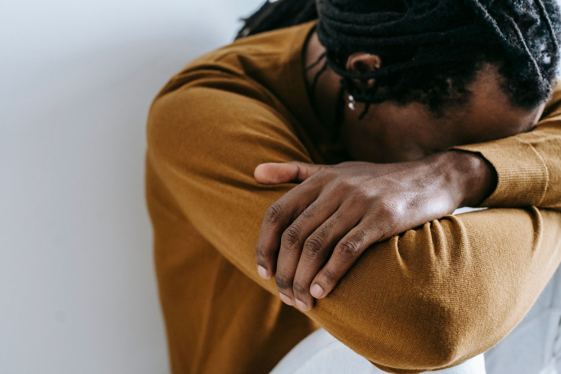 Person resting head on crossed arms, wearing a mustard sweater, appearing tired or upset.