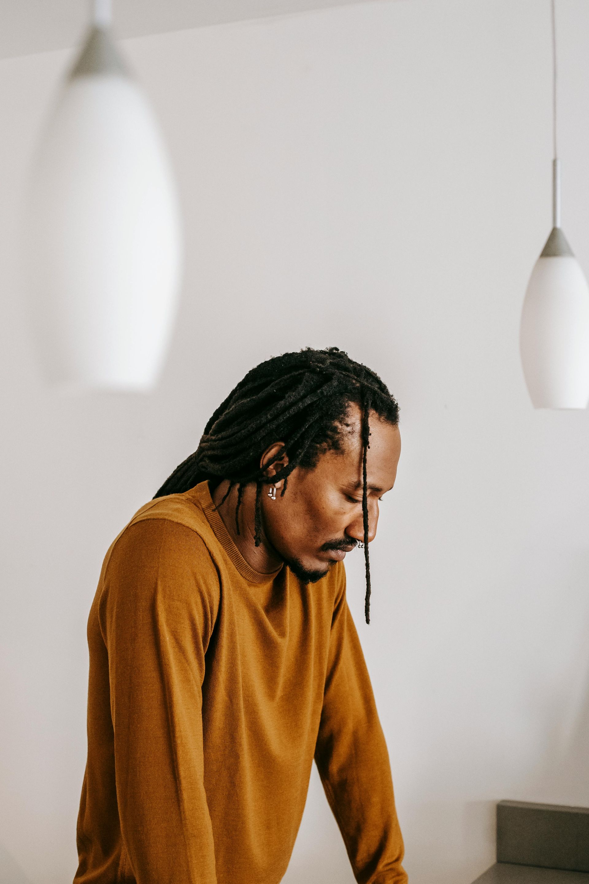 Person in a mustard sweater looking down in a minimalist room with hanging pendant lights