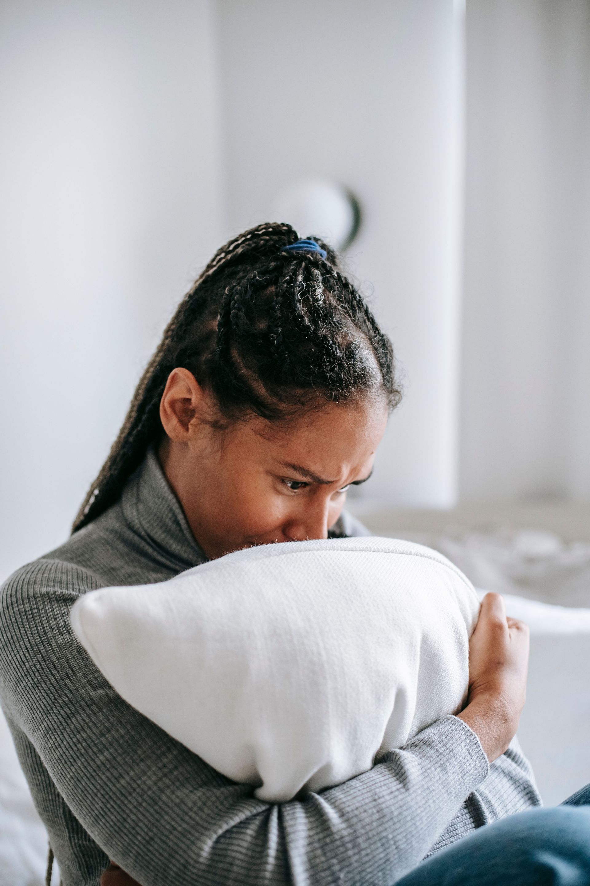 Person hugging a white pillow and looking down in a softly lit bedroom