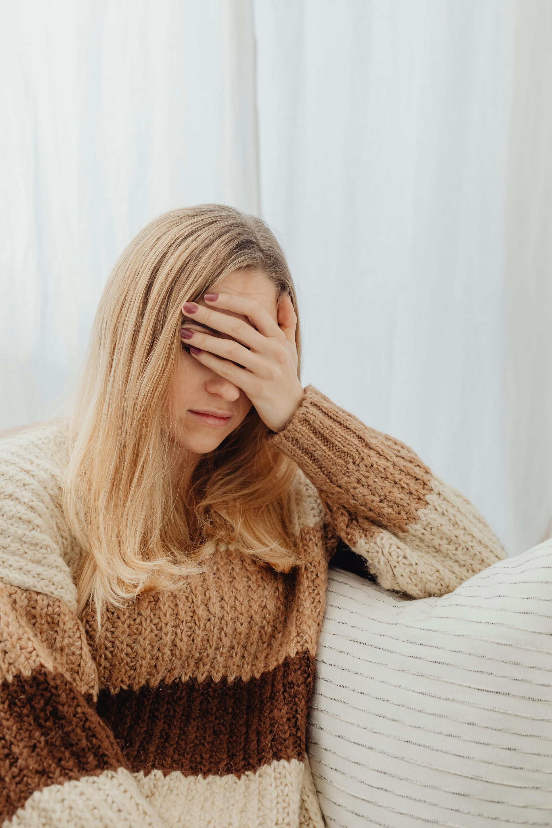 Person in a striped sweater sitting on a couch, covering their face with one hand.