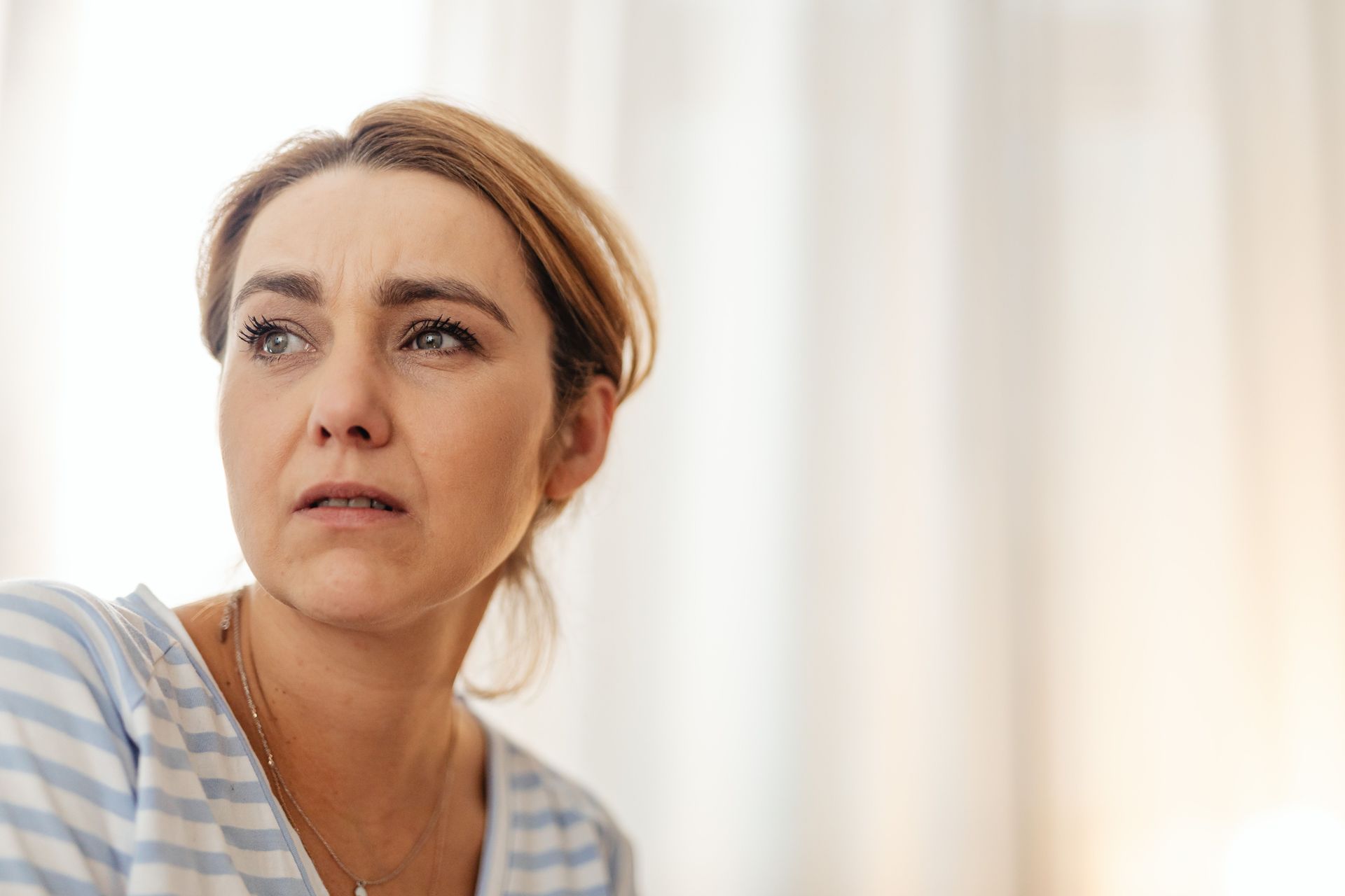 Woman in a light blue striped shirt looking off to the side with a concerned expression indoors