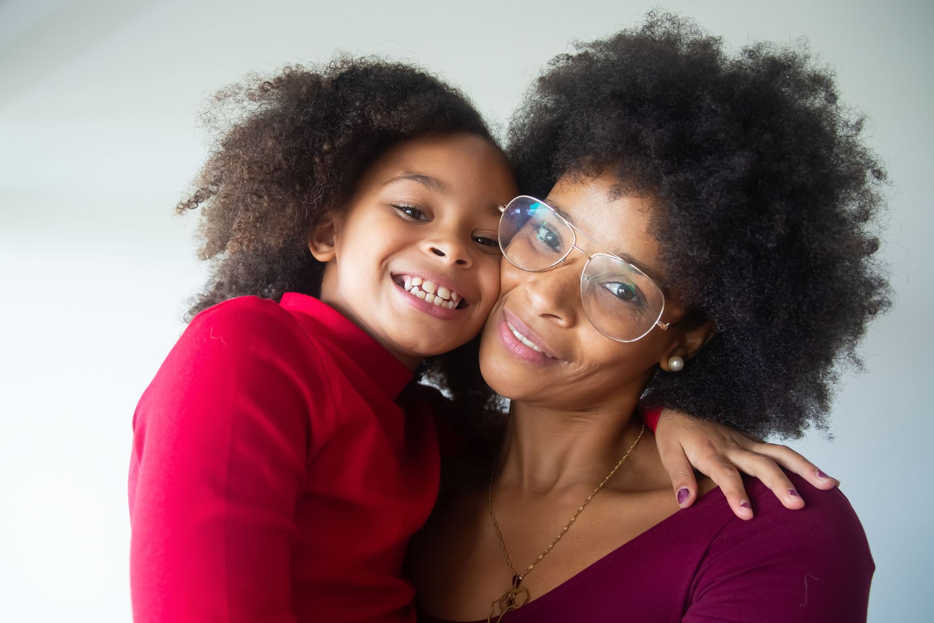 Smiling adult and child hugging, both with curly hair, against a bright white background