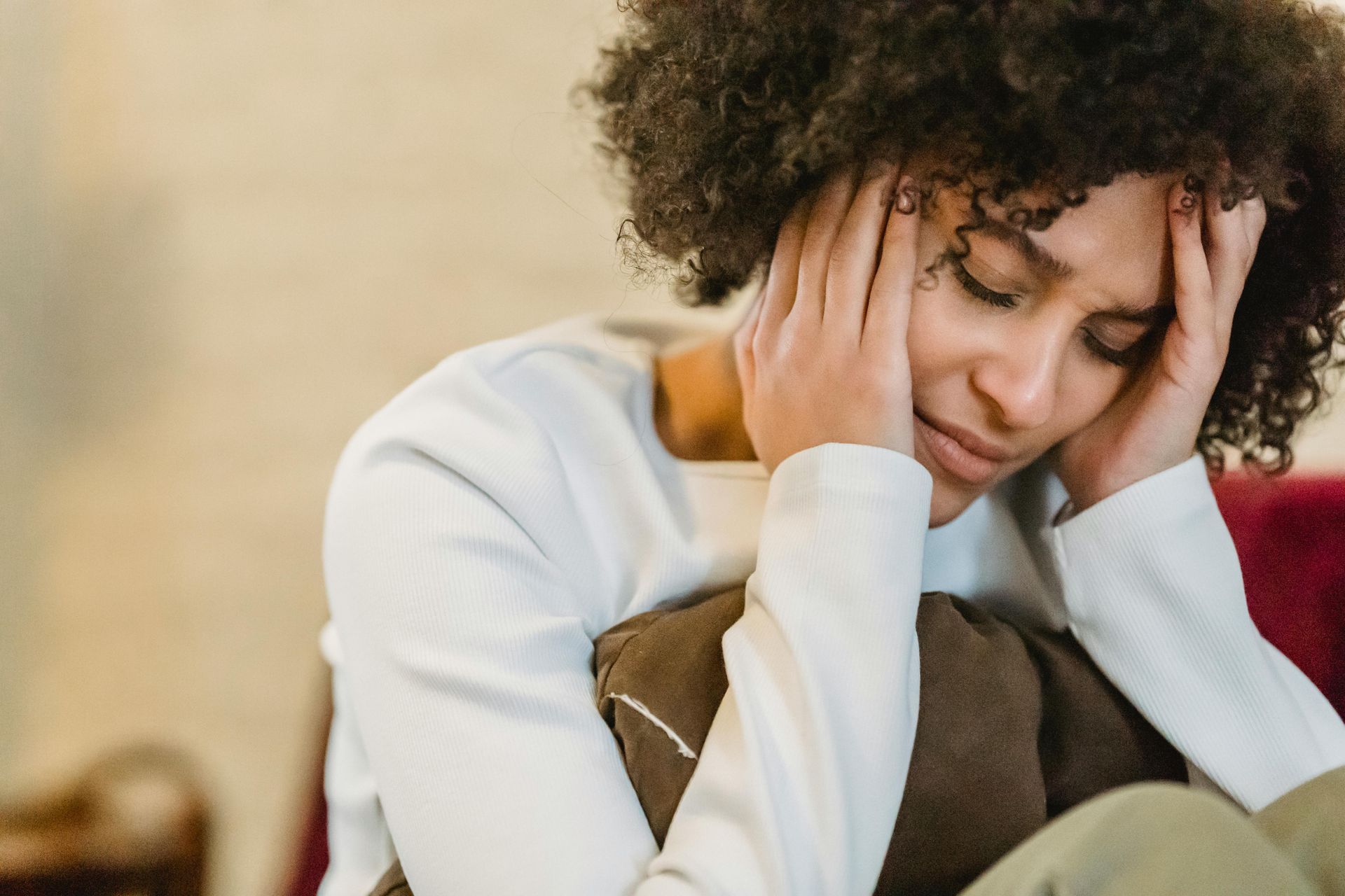 Person holding head in hands, looking distressed while sitting with a pillow
