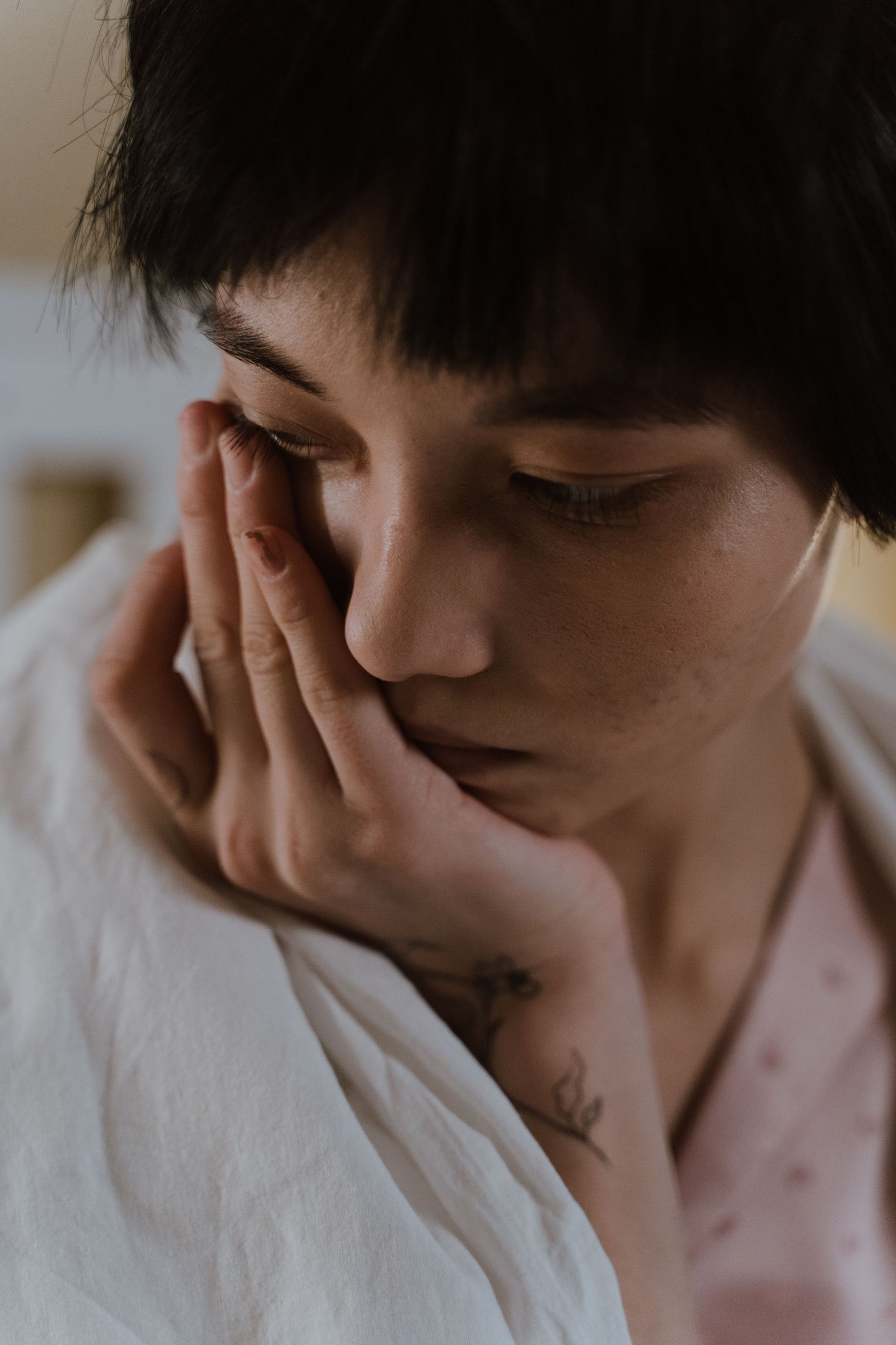 Person resting their face on their hand, looking down in a soft-lit close-up.