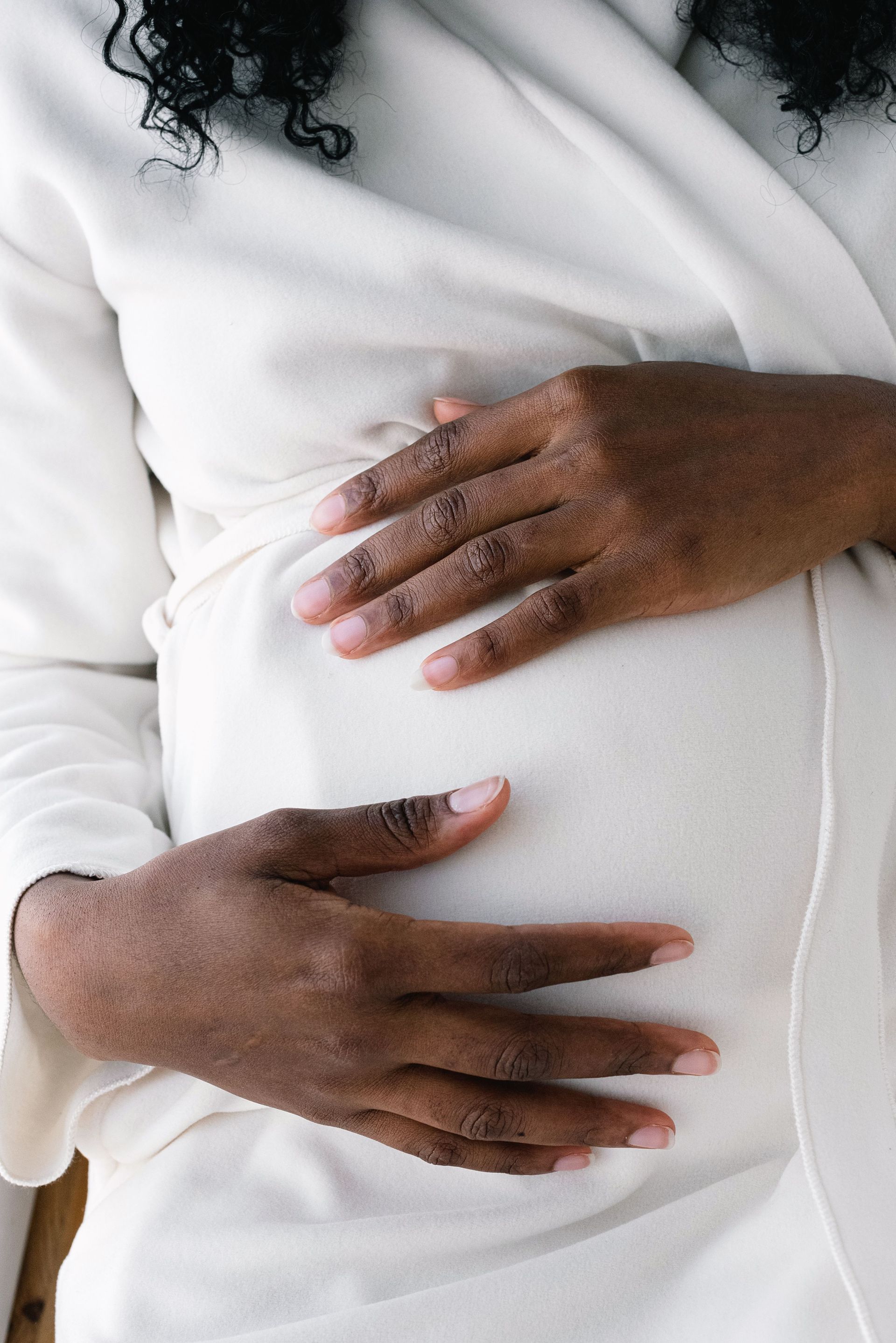 Two hands gently resting on a pregnant belly under a white shirt