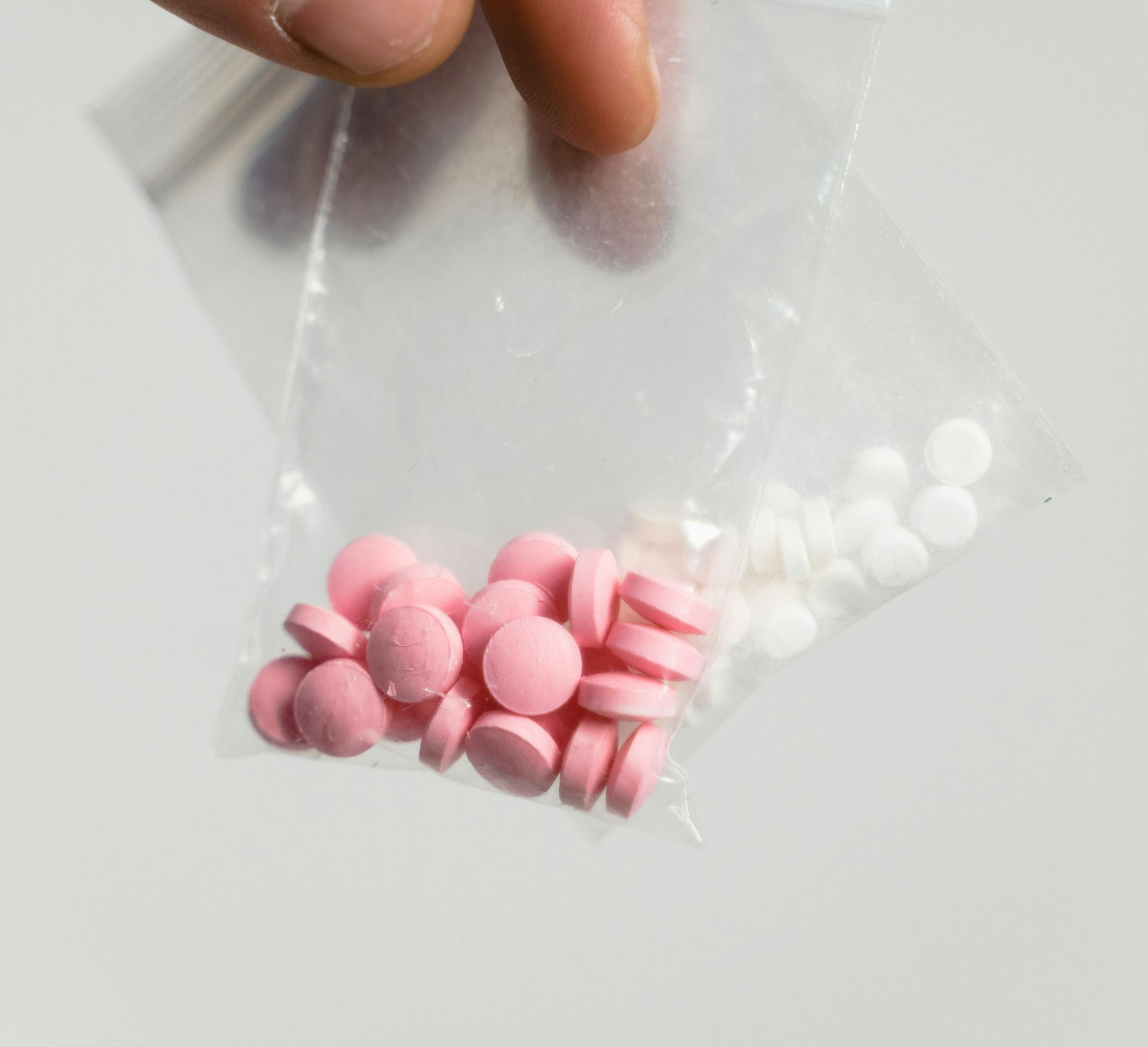 Hand holding a small clear bag with pink and white tablets inside