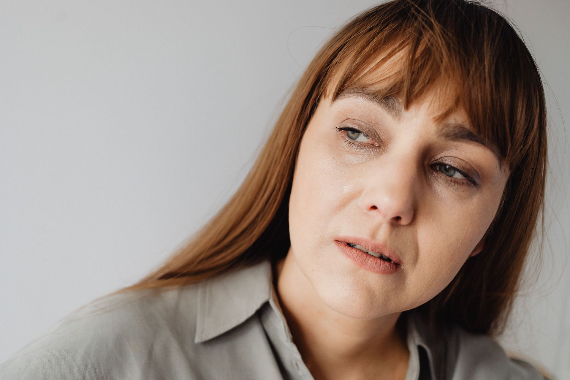 Close-up of a woman in a gray shirt looking off to the side with a sad expression