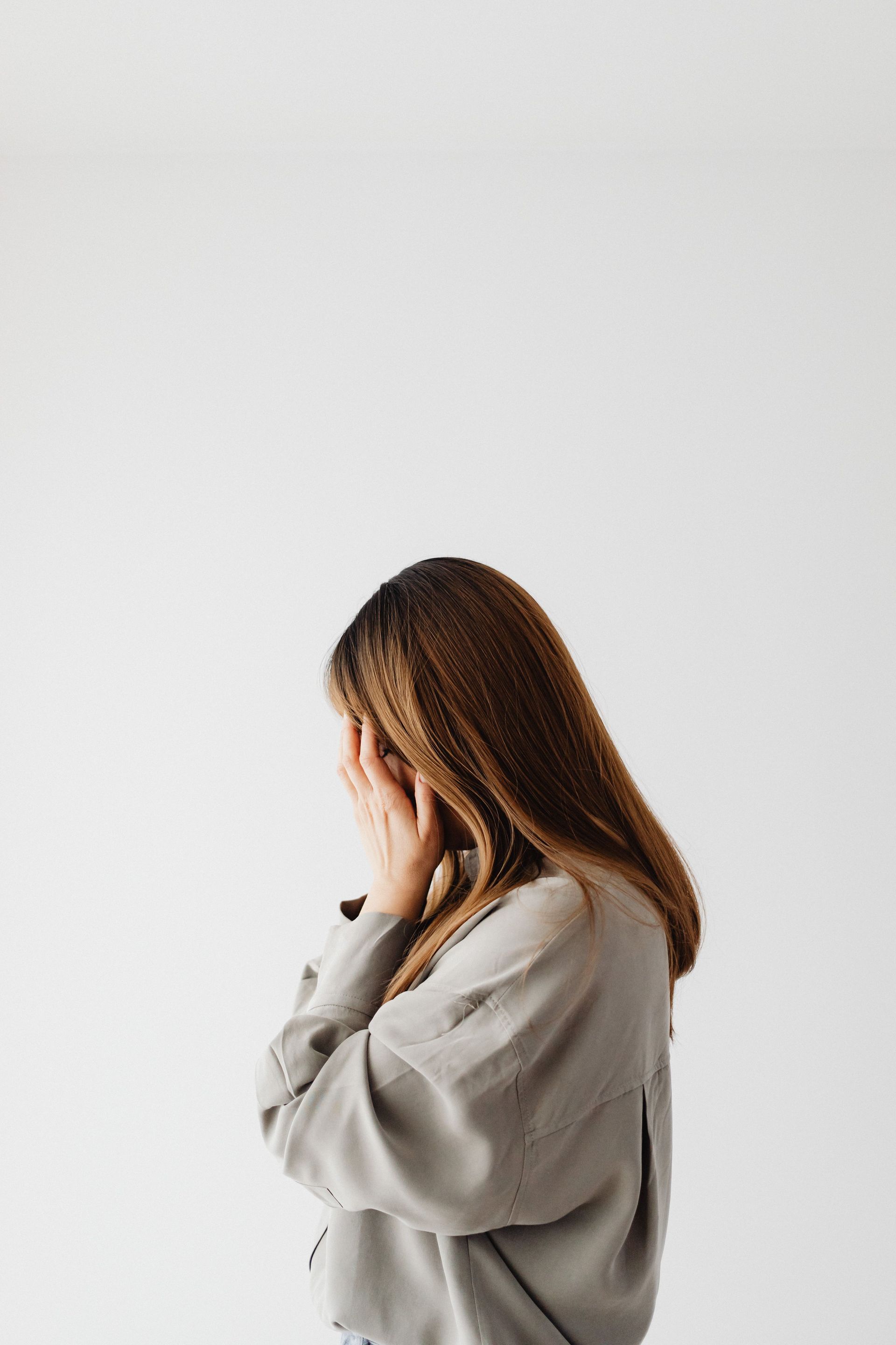 Woman in a gray sweater looking down against a plain white background