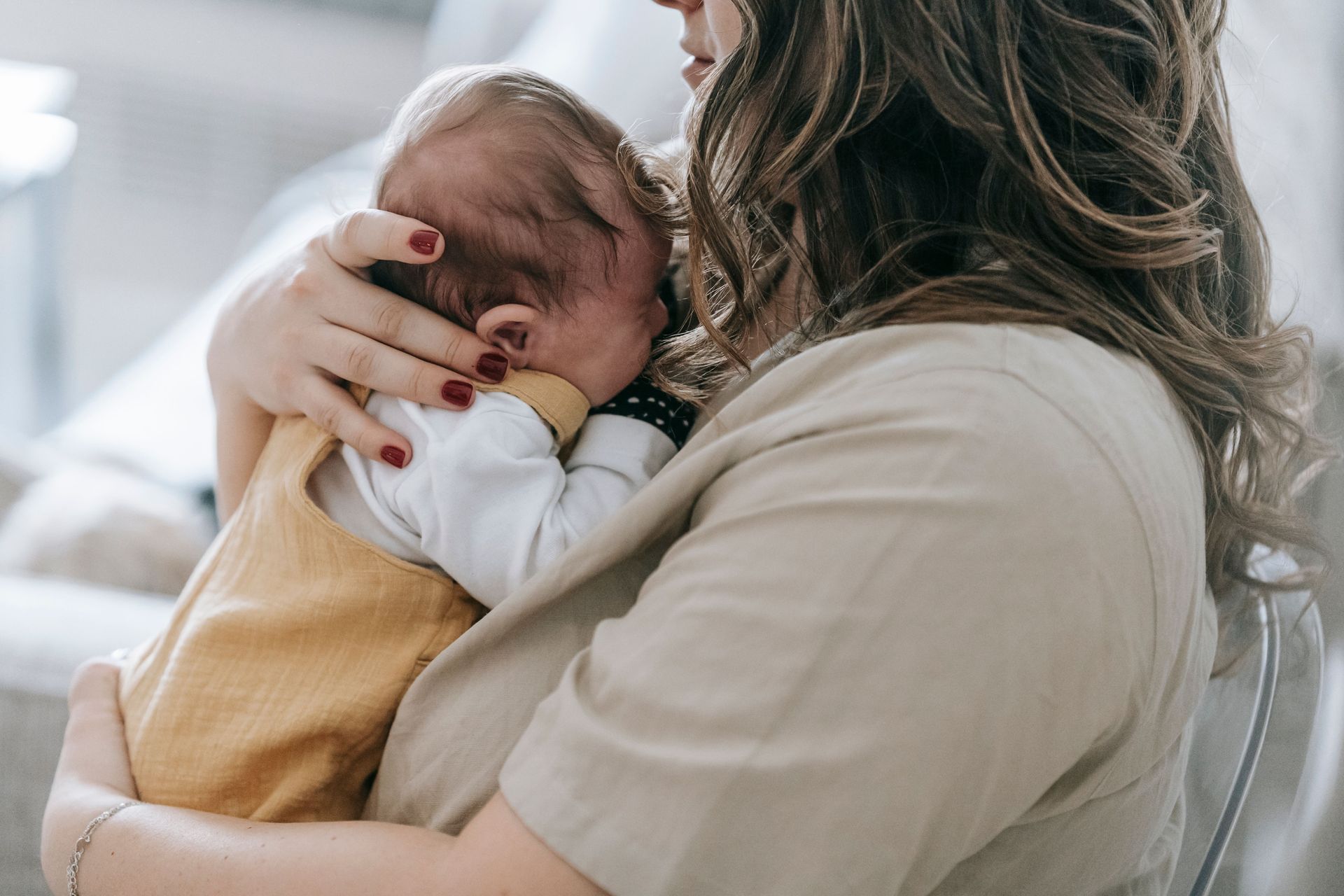 Woman cradling a sleeping baby against her shoulder in a bright indoor setting
